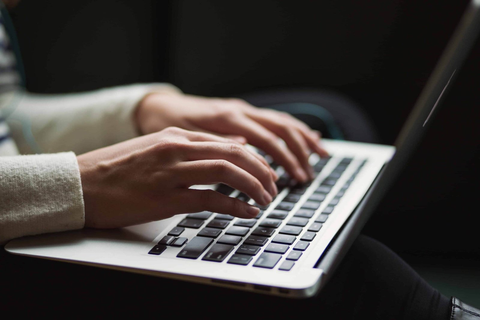 A person wearing a long-sleeved cream outfit sits with a laptop on their thighs, deeply engrossed in typing something.