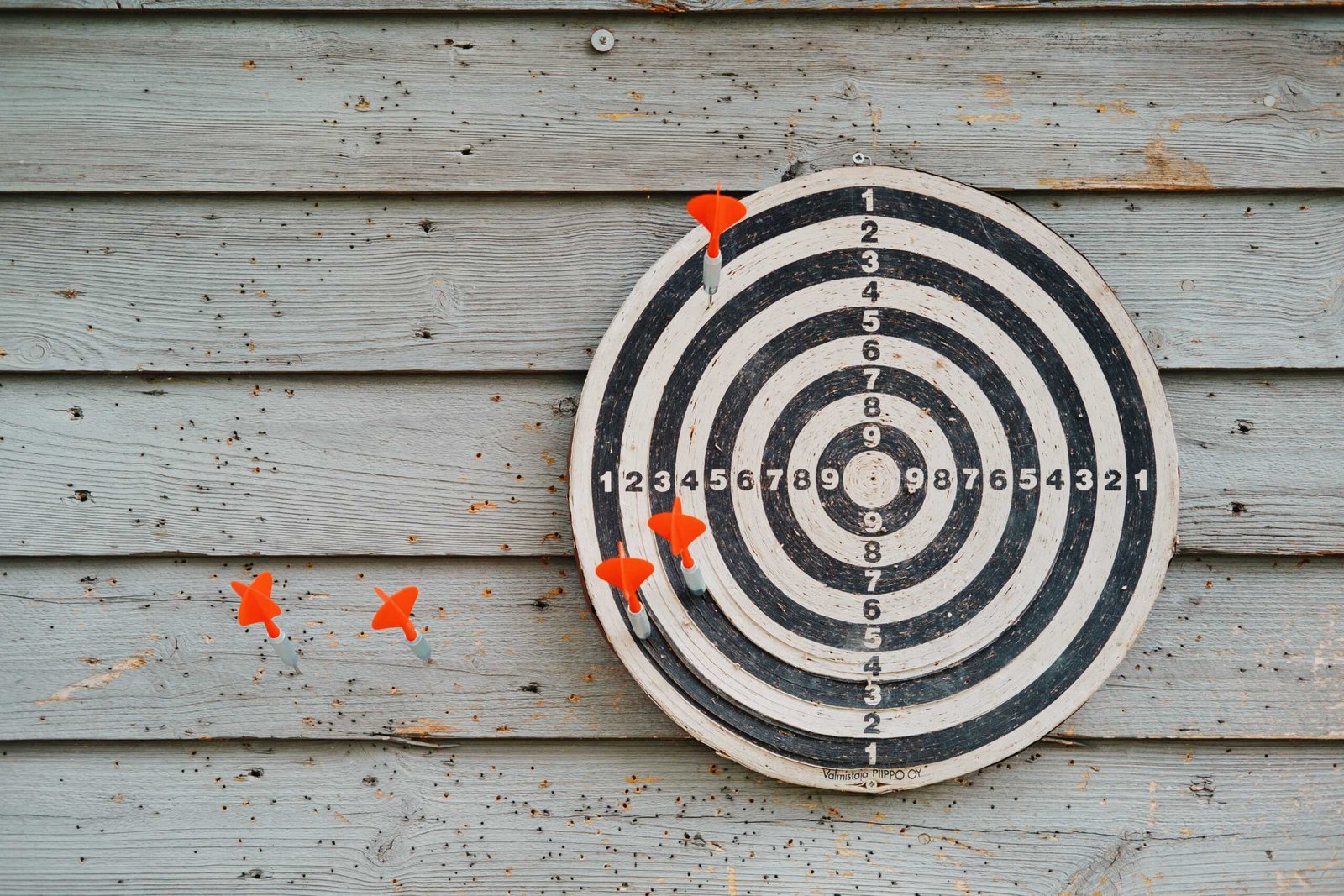 A dartboard with five darts hanging on a platform.