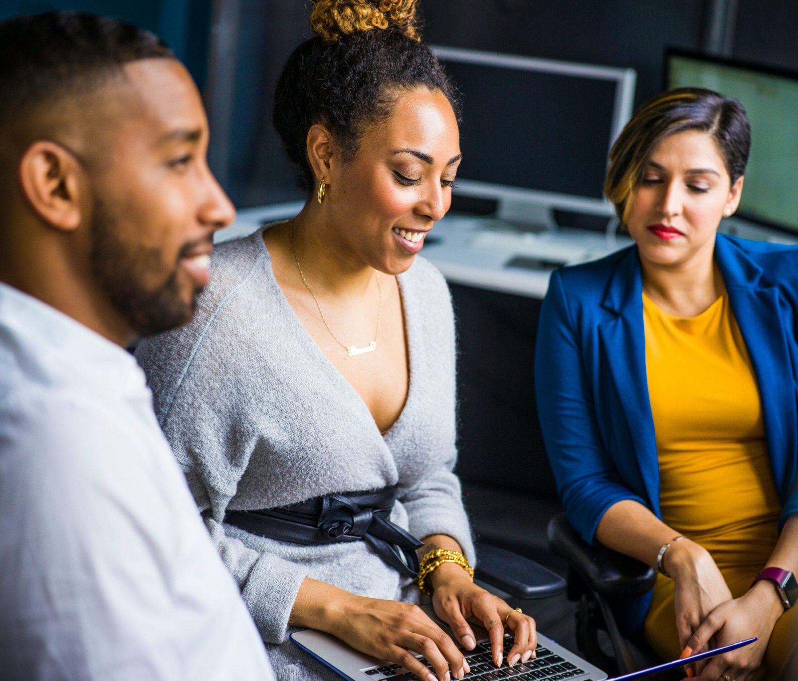 Two women and one man engage in conversation in front of a laptop