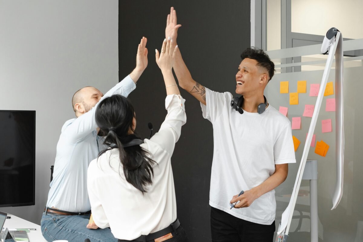 Three individuals celebrating with high fives, one standing while the other two are seated on the table.