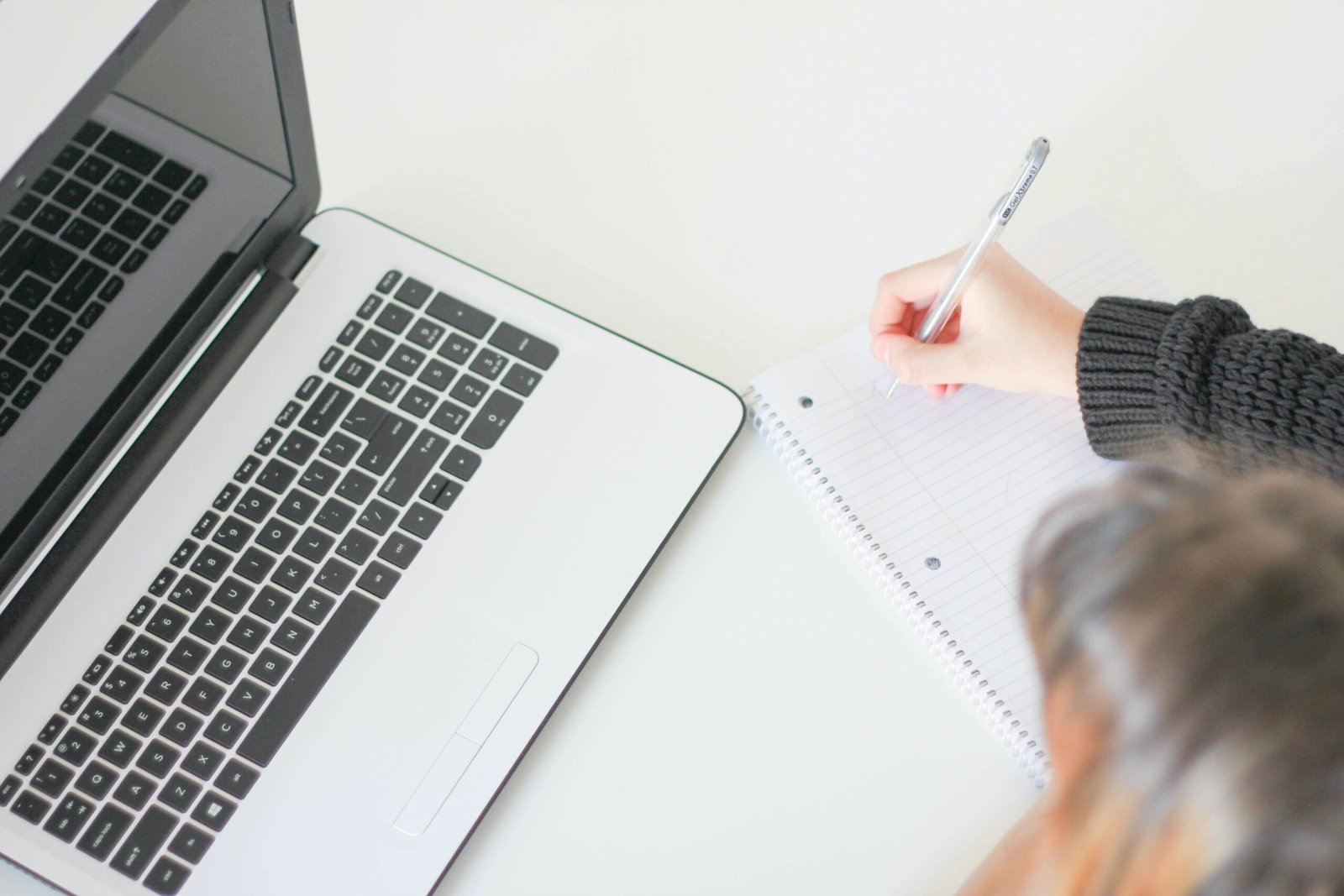 A woman wearing a smile and eyeglasses in a white suit sits in front of her laptop, handing papers to someone.