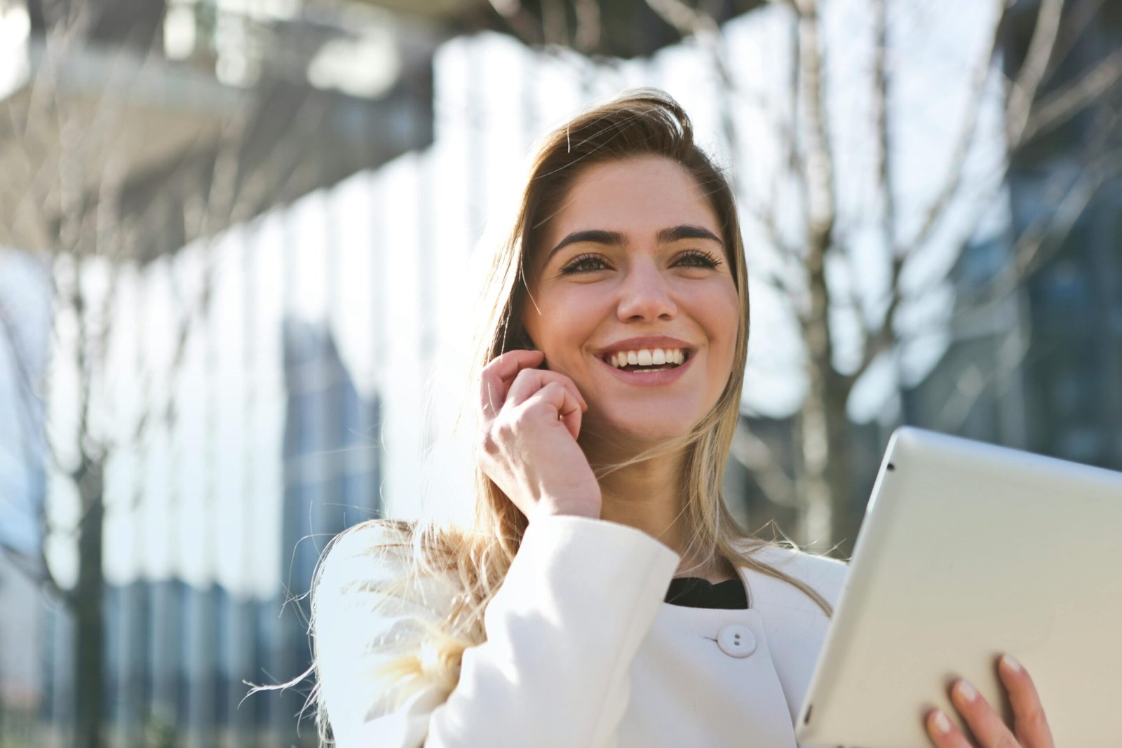 A woman wearing a smile and eyeglasses in a white suit sits in front of her laptop, handing papers to someone.